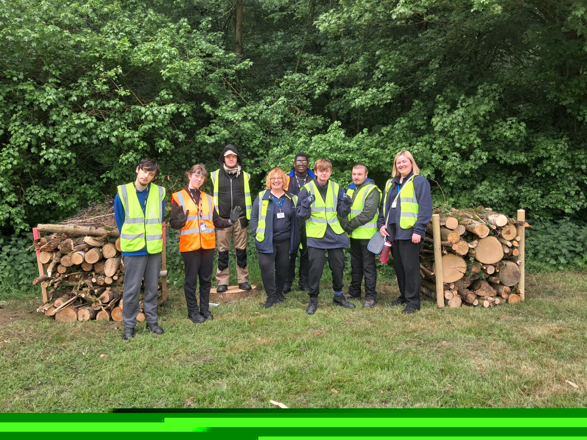 Picture of students in high vis gear standing next to Alice Mullan from Iron Mountain by log piles